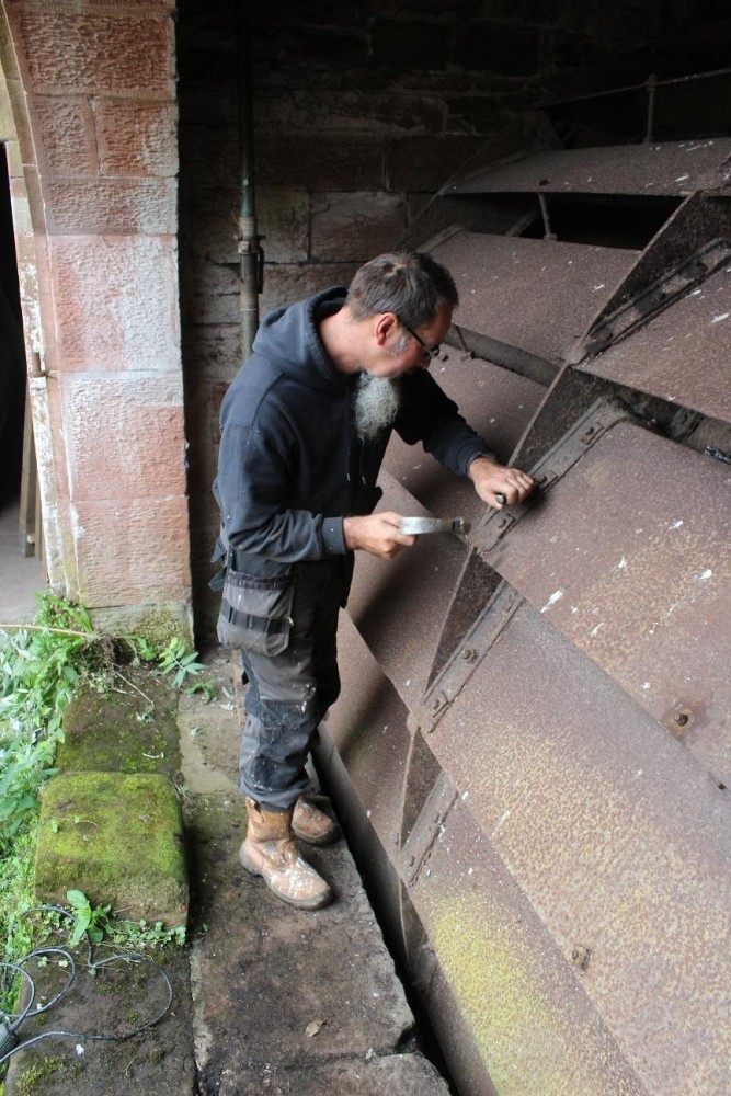 man undoing bolts on waterwheel